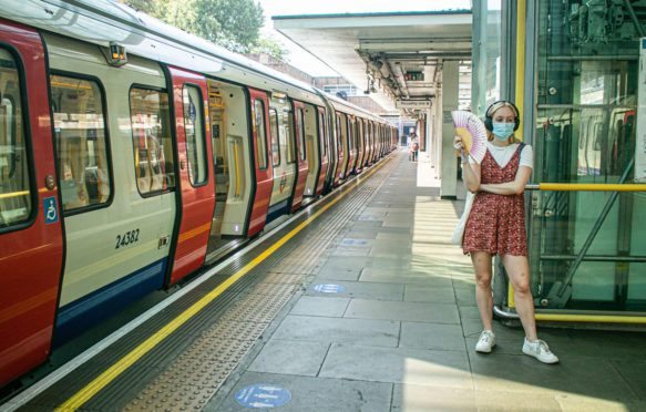 伦敦地铁乘客戴着面罩站在平台使用风扇来降温的炎热和潮湿的条件下在8月热浪。