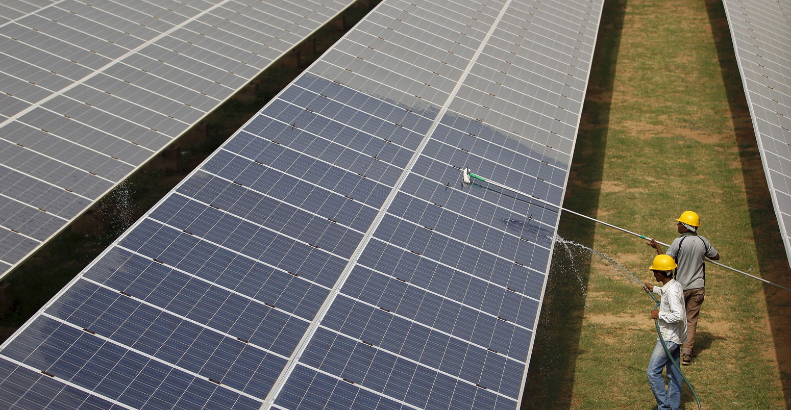 在印度古吉拉特邦，工人们正在清洁太阳能发电厂内的光伏板。