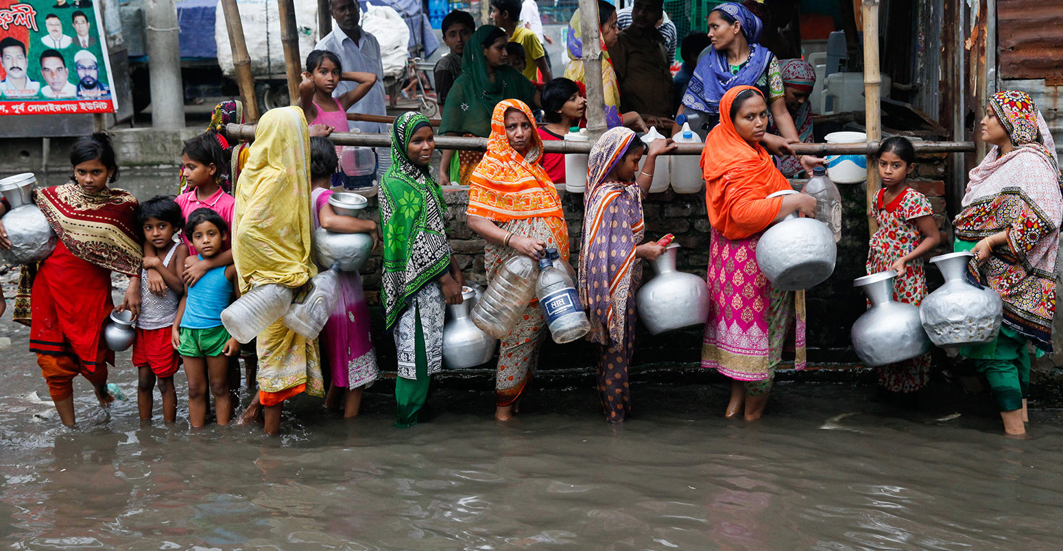 2017年6月，孟加拉国达卡，妇女和儿童在积水地区收集饮用水。图片来源:Mehedi Hasan/Alamy Stock Photo。