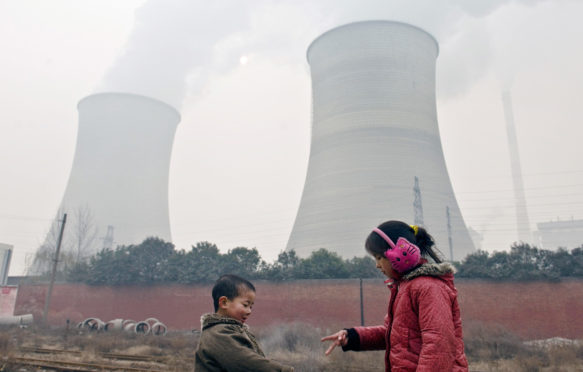 两个小孩玩猜拳游戏靠近冷却塔和烟囱在中国洛阳市燃煤发电厂吸烟