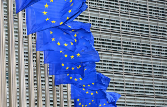 欧盟总部Berlaymont大楼外，一排飘扬的蓝色欧盟旗帜